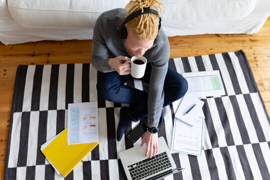 Albino african american man sitting on the floor and working from home using laptop