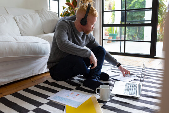 Albino african american man sitting on the floor and working from home using laptop
