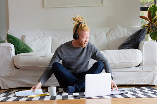 Albino african american man sitting on the floor and working from home using laptop