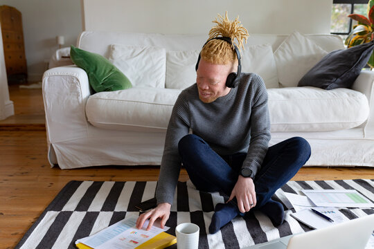 Happy albino african american man sitting on the floor and working from home using laptop