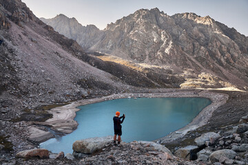 Hiker tourist taking photograph of mountain lake at sunset