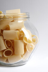 Glass jar filled with dry paccheli yellow pasta over isolated white background. Rigatoni pasta in a glass apothecary jar.