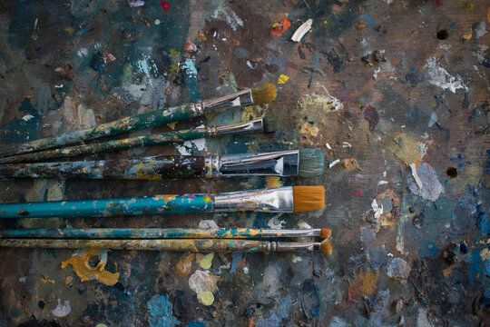 Different sized, used acrylic paintbrushes on a wooden table, filled with paint stains