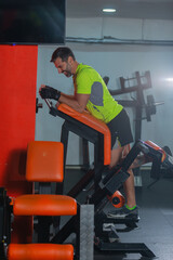 Side view of a middle-aged man with a yellow fluorescent shirt exercising on the machine for legs.