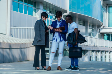 Businessman showing documents to his multi-ethnic co-workers in front of their big modern office building