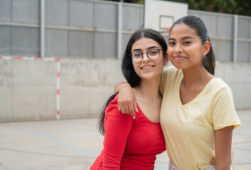 Two Student teenager girls from different races outside high school. Portrait of multiracial female friends in a playground. 