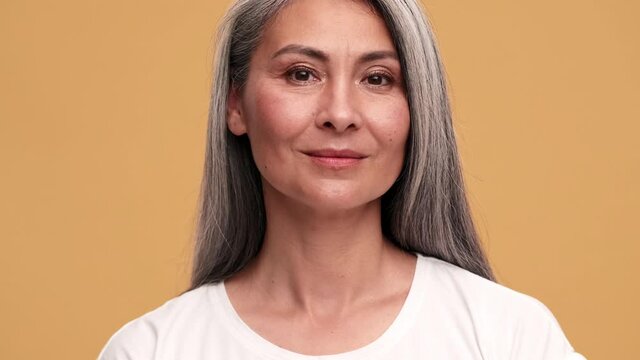 A smiling asian mature woman opening her eyes at the camera in the beige studio