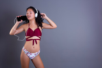 Young chinese girl in bikini listening to music from smart-phone and headphones