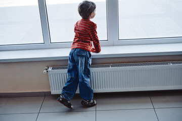 Cute boy waiting at the airport looking at window and enjoying planes arriving, rear view