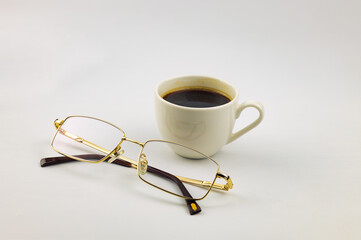 A cup of coffee and eyeglasses are on the table. White background.