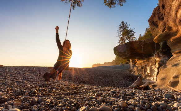 Adventurous White Caucasian Woman on a swing at Sandcut Beach on the West Coast of Pacific Ocean. Summer Sunny Sunset. Canadian Nature. Located near Victoria, Vancouver Island, BC, Canada.