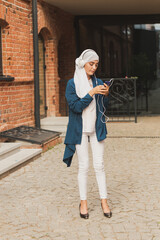 Portrait of young modern arabian woman holding mobile phone and listening the music to headphone.