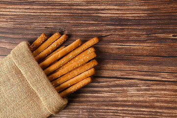 Grissini are in sackcloth. Crispy white sticks on a brown background. With sesame seeds. The appetizer is delicious.