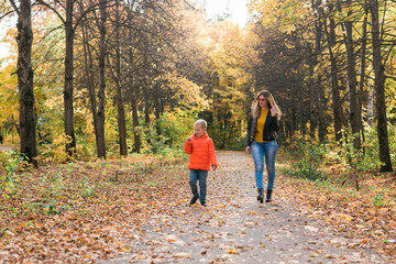 Obraz premium Mother and son walking in the fall park and enjoying the beautiful autumn nature. Season, single parent and children concept.