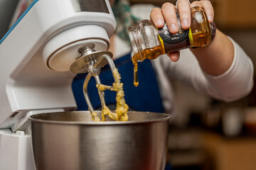 Close up view of woman's hand putting honey from jar on bowl of an electric mixer for the...