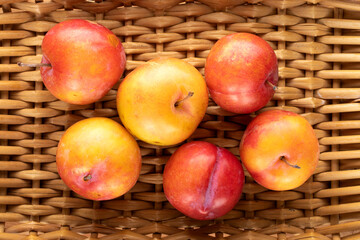 Several juicy sweet yellow-red plums on a vine mat, close-up, top view.