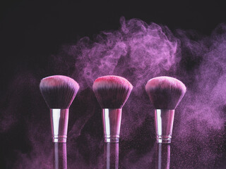 Make-up brush with purple powder explosion on black background