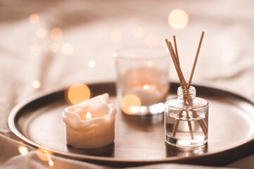 Home perfume in glass bottle with wood sticks, scented burn candles  tray in bedroom close up....