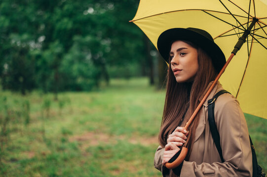 Woman holding yellow umbrella while walking in the park during rain
