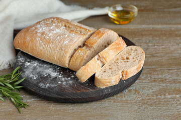 Cut delicious ciabatta with rosemary on wooden table