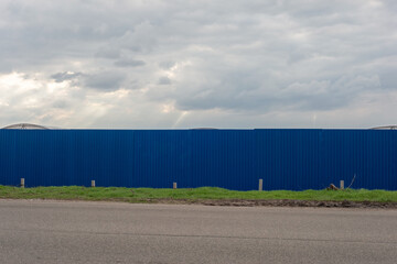 Fototapeta na wymiar blue fence with trees near the road. Spring 2021
