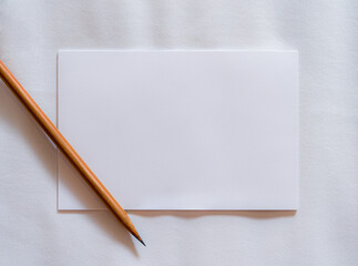 Blank white note paper and pencil on white fabric cloth background