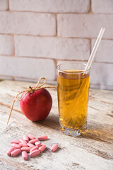 Scattered pills, glass of fresh juice with straw and an apple. Choice of healthy life. Vertical photo