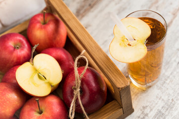 Wooden tray full of ripe red apples and glass of juice with straw and apple slice