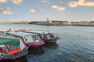 Fototapeta na wymiar view of tourist boats and a warship on the Neva River in St. Petersburg against the blue sky and the city