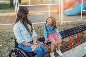 A mother in a wheelchair enjoys with her daughter outside on a beautiful sunny day.