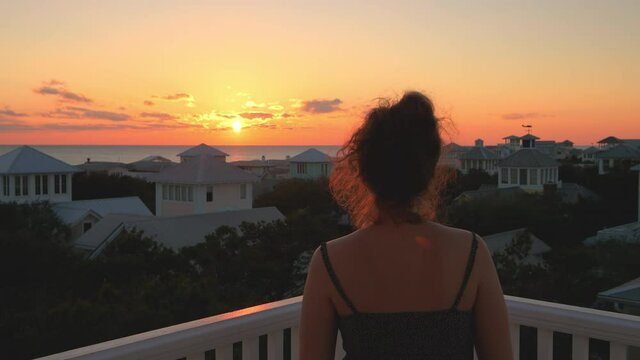 View on colorful sunset with young woman watching photographing taking picture with phone Gulf of Mexico in Seaside, Florida on wooden rooftop terrace building house balcony