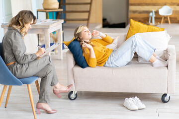Woman psychologist takes in her office. Session by teenage girl. Teenage girl lies on couch.