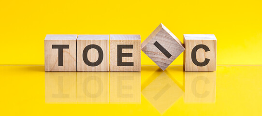 TOEIC word is made of wooden building blocks lying on the yellow table, concept