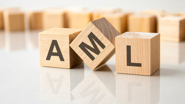 three wooden cubes with the letters AML on the bright surface of a gray table, business concept
