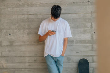 Obraz na płótnie Canvas teenage boy with mobile phone and skateboard on the wall
