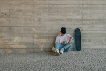 teenage boy with mobile phone and skateboard on the wall