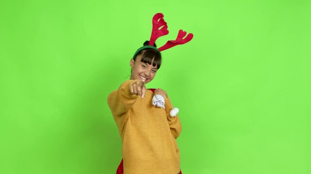 Young woman with christmas hat points finger at you with a confident expression over isolated background. Green screen chroma key