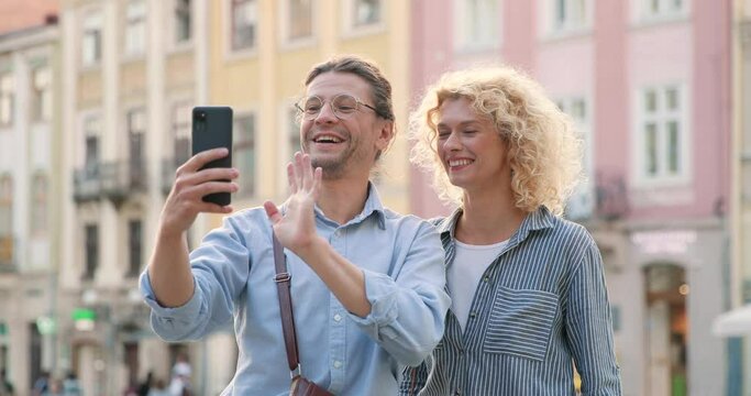 Waist up portrait view of the caucasian man and woman in love chatting with somebody via video call and gesturing with happy emotions