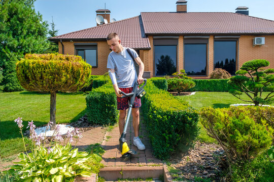 Young man with amputated arm and prosthesis removing weeds on the sidewalk of a backyard garden with a cordless grass trimmer