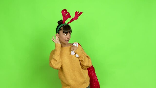 Young woman with christmas hat listening to something by putting hand on the ear over isolated background. Green screen chroma key