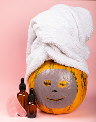 copy for space, pumpkin with towel and mask on pink background, face care product, asexuals for girls, cosmetic bottles