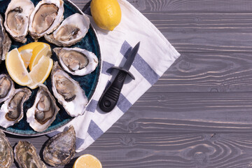 Open oysters with lemon on a beautiful blue plate, on a textured wooden background.