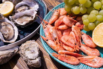 resh oysters with lemon slices on a platter, shrimp with grapes on a platter, on a wooden background.