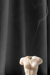 Candle in woman torso shape burning in grey interior in slow motion, atmosphere and smoke after candle