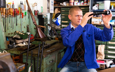 Portrait of professional craftsman engaged in adjusting optical sight in weapons workshop.