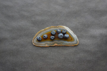 Flat lay of red agate gemstone and juicy, fresh blueberries on black table. Isolated sweet bilberry fruits on translucent crystal surface on grey background. Copy Space. Healthy raw vegetarian food 