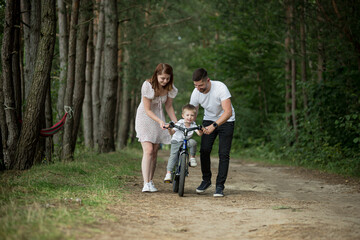 Fototapeta premium Young family on a picnic in the woods, husband, wife and young child son, teach son to ride a bicycle