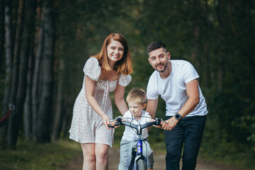 Fototapeta na wymiar Young family on a picnic in the woods, husband, wife and young child son, teach son to ride a bicycle