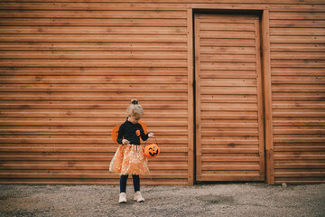 Cute little girl wearing witch costume holding pumpkin bucket with candies on Halloween. Trick or treat.