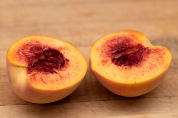 Carved in half fresh Angelus peach fruit on a wooden cutting board 